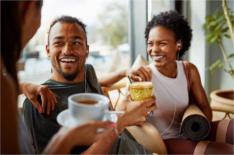 Friends laughing over drinks at a cafe, two of them wearing Nuropod earpieces
