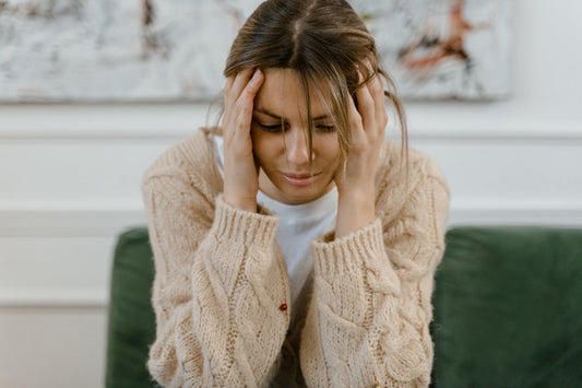 Woman sitting on a couch with her head in both hands, experiencing migraine pain