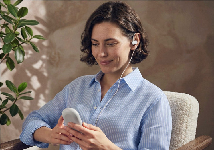 Woman using the Nuropod device, wearing it on her ear while holding the blue handheld controller