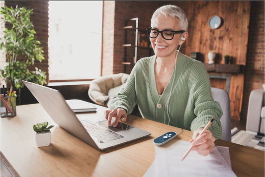 Woman wearing a Nuropod wearable auricular vagus nerve stimulation device with its controller while working at a laptop